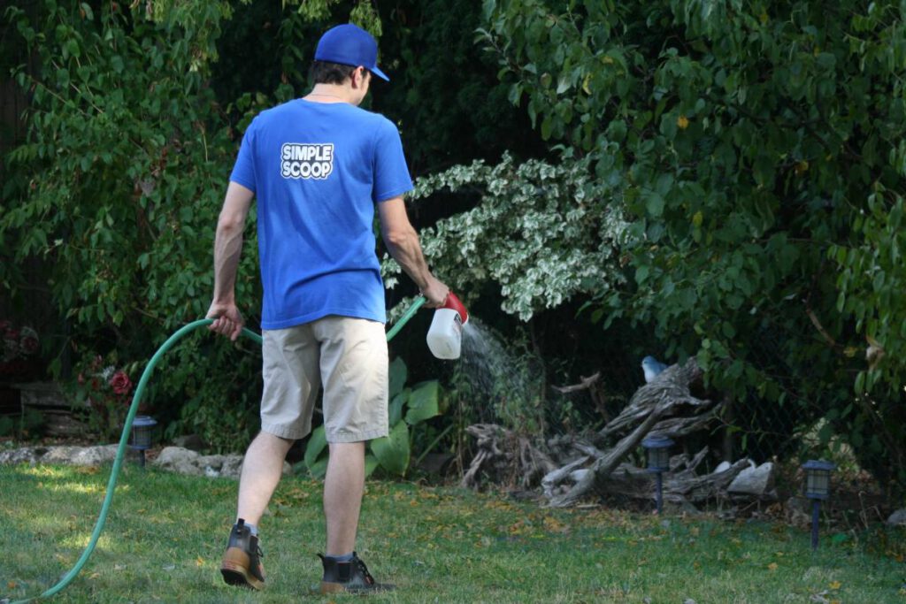 Person using a hose attachment to spray grass with environmentally-friendly deodorizer.