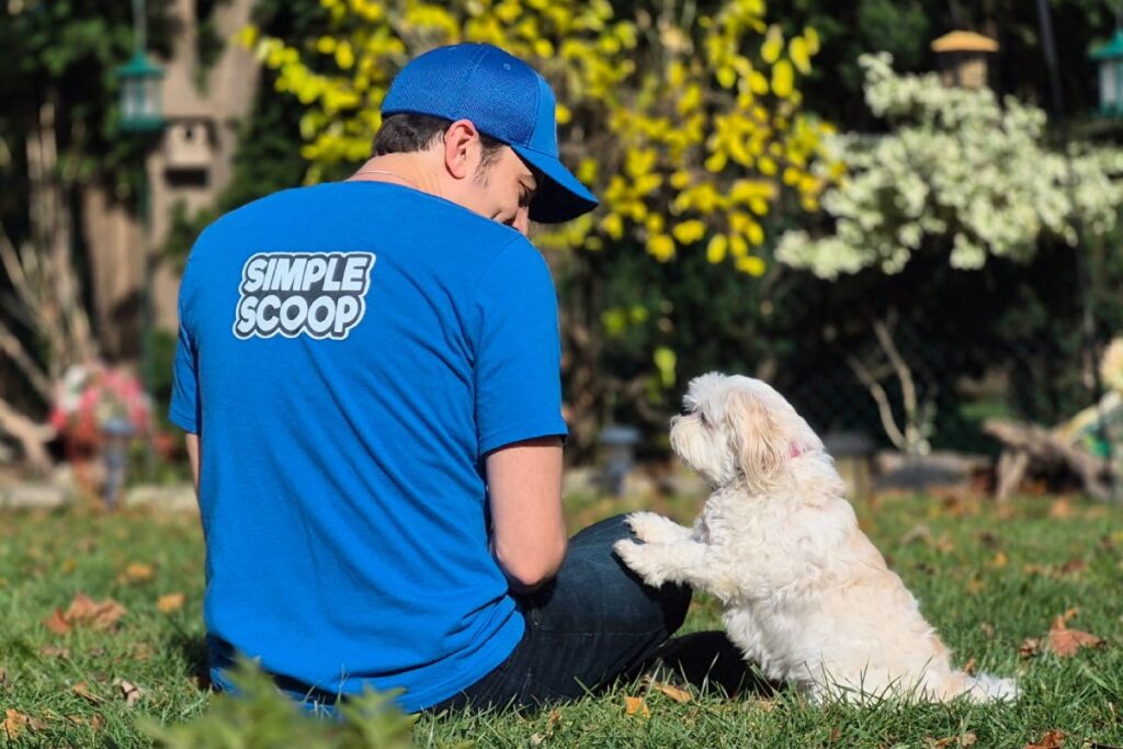 Person sitting on grass with a cute white dog.
